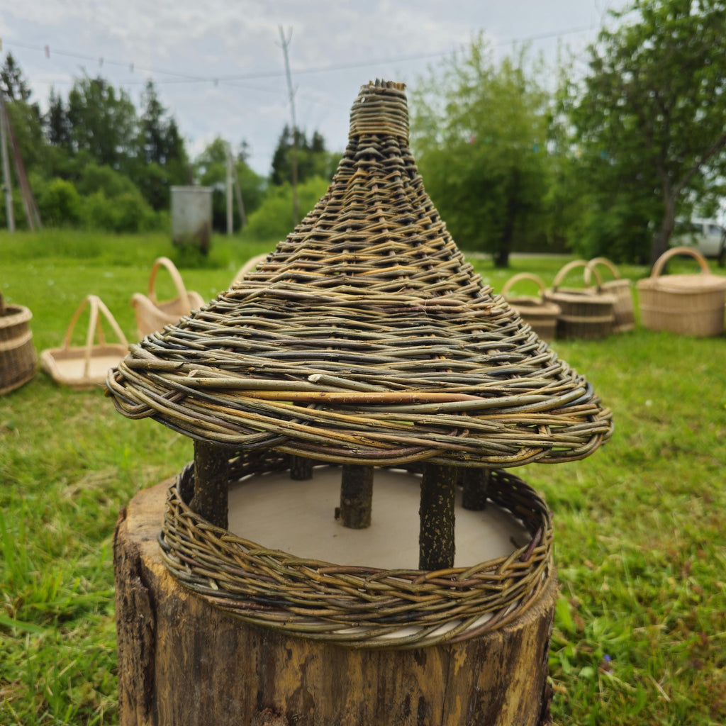 Woven straw lantern on a wooden base in an outdoor setting with greenery.