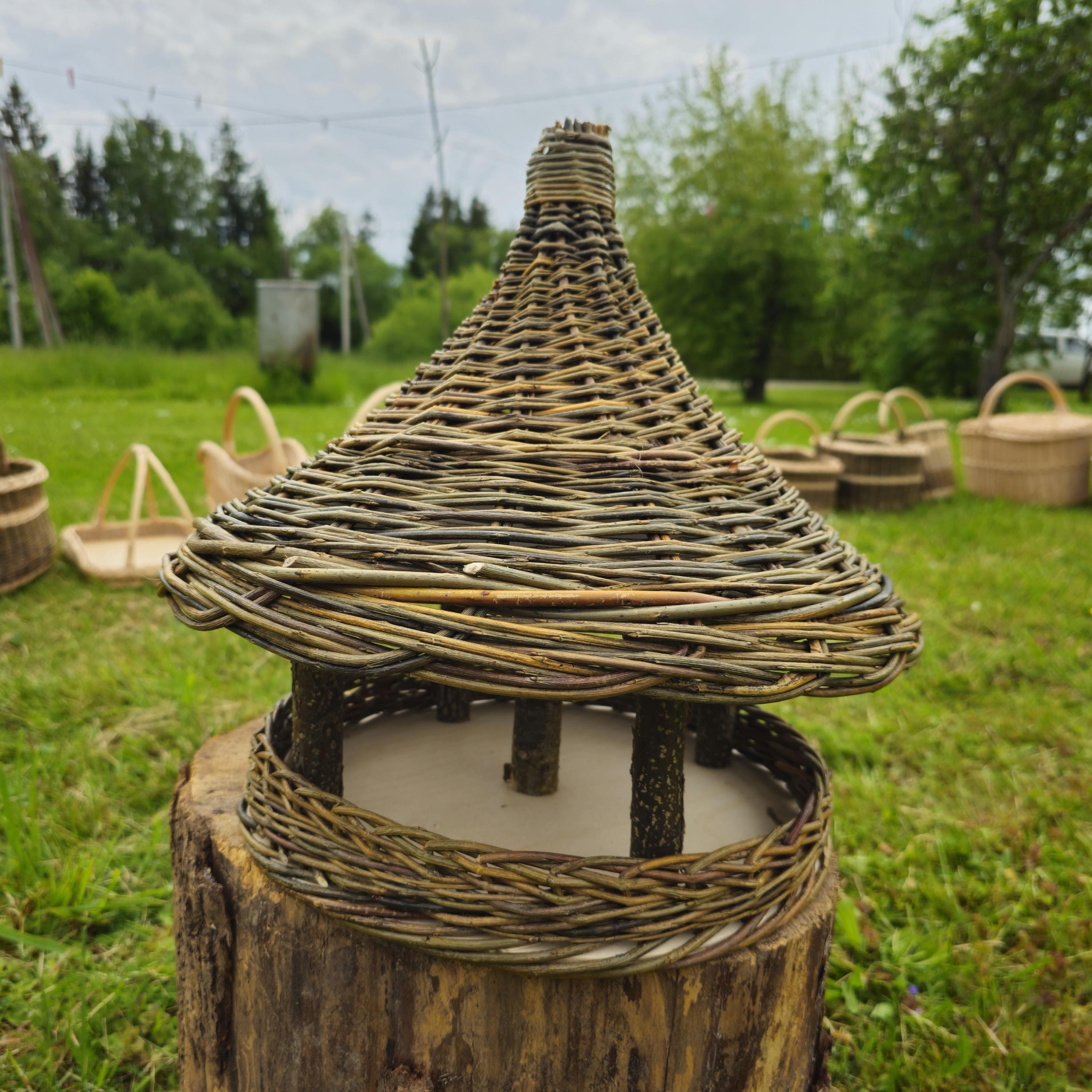 Woven straw lantern on a wooden base in an outdoor setting with greenery.